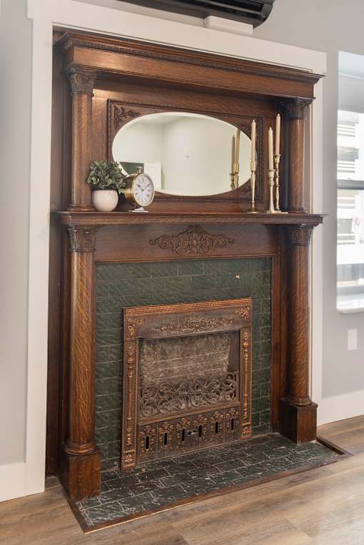 A fireplace with a mirror above it and a plant to the left.