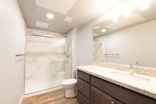 A bathroom with a marble shower, toilet, and sink.