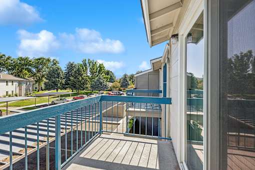 A balcony with a blue railing overlooks a parking lot and trees.
