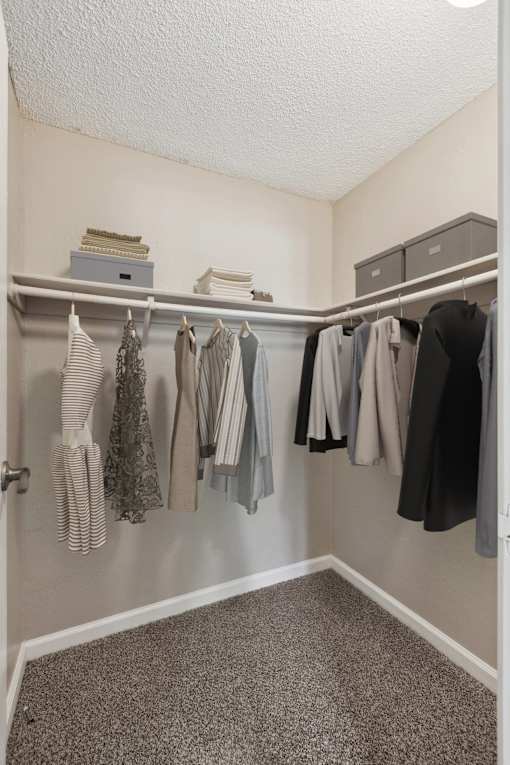 A closet with clothes hanging on a rail and a shelf above.