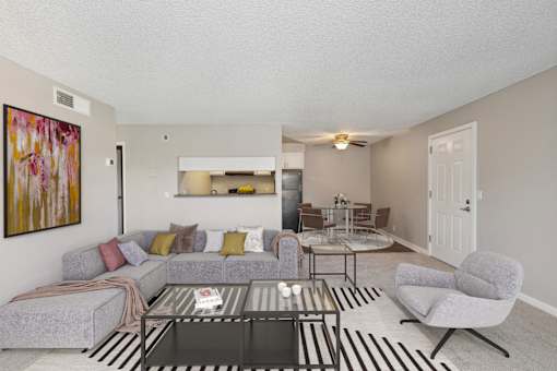 A living room with a grey couch, a glass coffee table, and a painting on the wall.