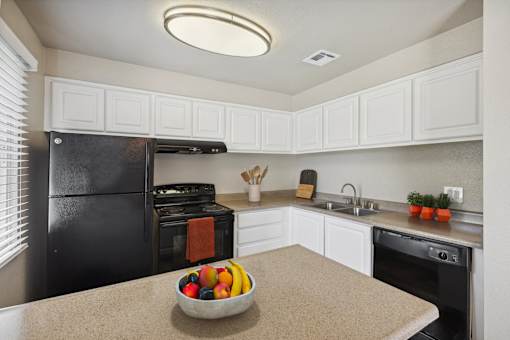 A kitchen with a black refrigerator, white cabinets, and a bowl of fruit on the counter.