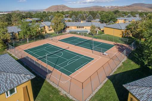 A tennis court surrounded by a fence and buildings.
