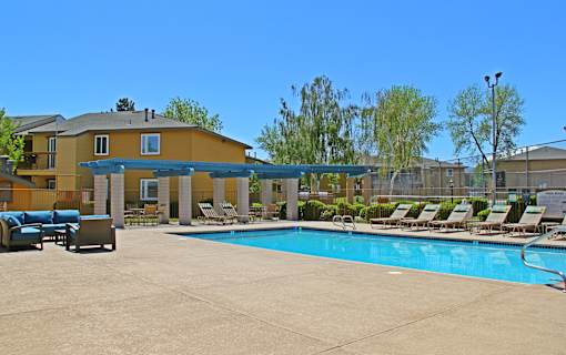 A large swimming pool in front of a yellow building with lounge chairs around it.