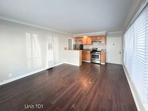 A spacious living room with wood flooring and a kitchen area in the background.