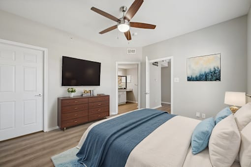 A bedroom with a bed, a ceiling fan, and a dresser with a flat screen TV mounted above it.