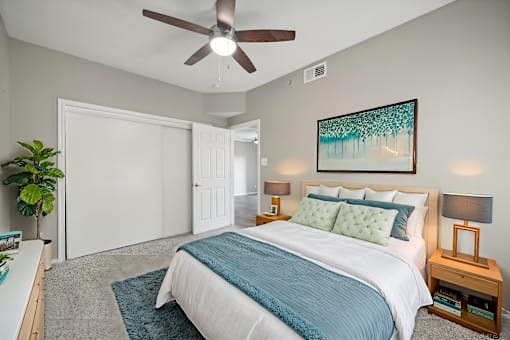 A bedroom with a bed, a ceiling fan, and a painting on the wall.