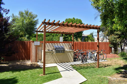 View of community grilling station with counterspace to prep food under a pergola and with bike rack near by