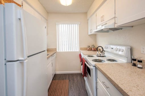 View of kitchen with wood like flooring, white cabinets, white appliances, and well lit window