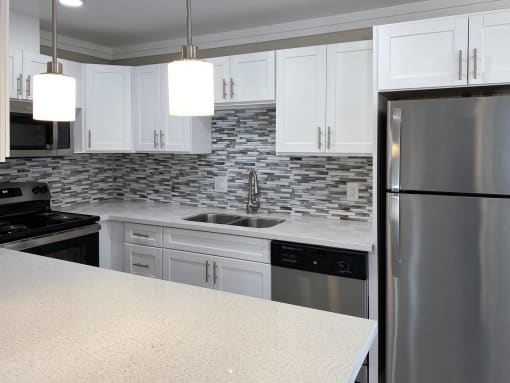 View of kitchen with stainless appliances, stone counter tops, white cabinets and recessed lighting