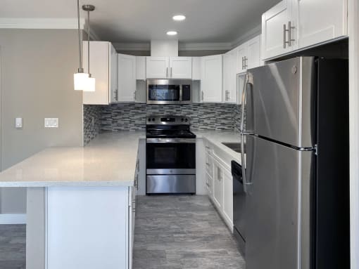 View of kitchen with stainless appliances, stone counter tops, white cabinets and recessed lighting
