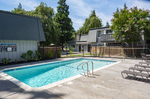 View of gated community pool with lounge chairs and view of exterior of buildings in background