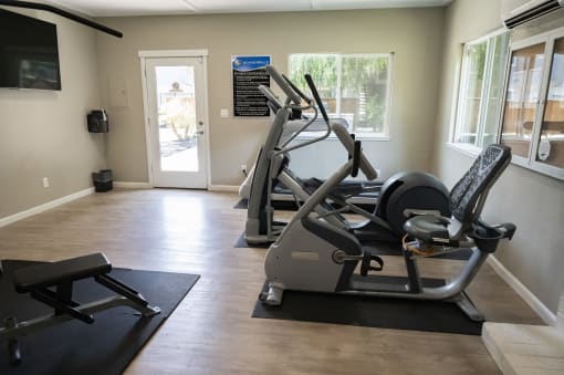 View of community fitness center with stationary bike, elliptical, treadmill and will lit window