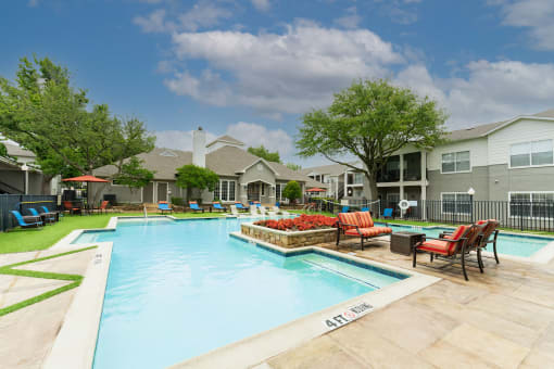 View of pool area with lounge chairs, sitting area, exterior of backside of leasing office, lush grass and trees