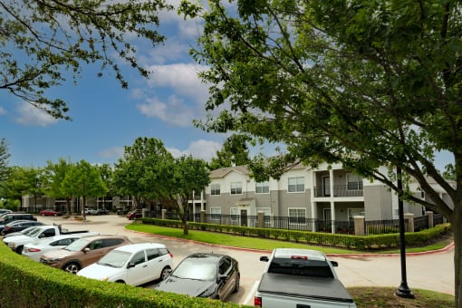 view of exterior of building and parking area with lush shrubbery and trees