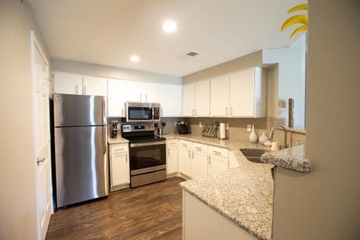 Alternate kitchen view with stainless appliances, white cabinets, stone counters, and wood look flooring