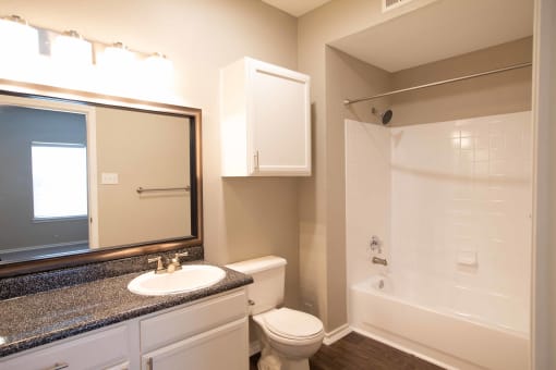 View of bathroom with large vanity, sink, large mirror, white cabinets, toilet, tub shower combo, and wood like flooring