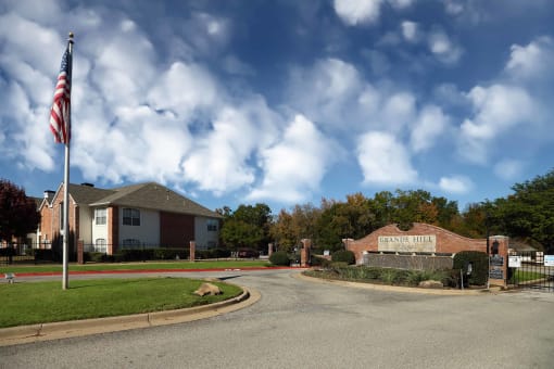 View of front entry gate with engraved Grande Hill Estates logo engraved in front entry water fall flower bed. Shows exterior building and American flag in back ground.