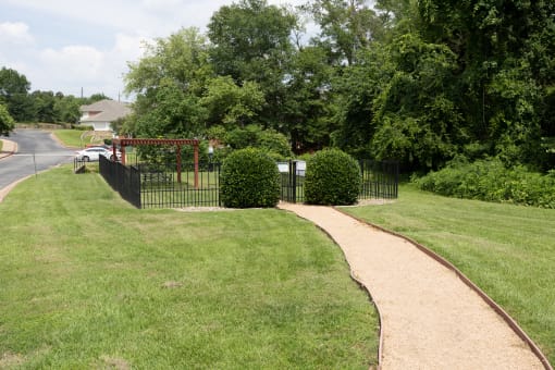 View of gated dog park with pergola and seating underneath and wooded area in background