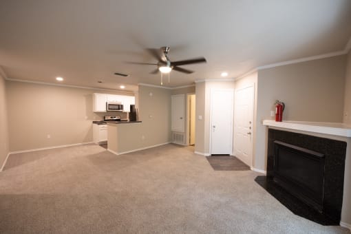 View of Tuscany from living area with carpet flooring, gas fireplace, ceiling fan and view of kitchen with white cabinets, dark counters, and stainless appliances.