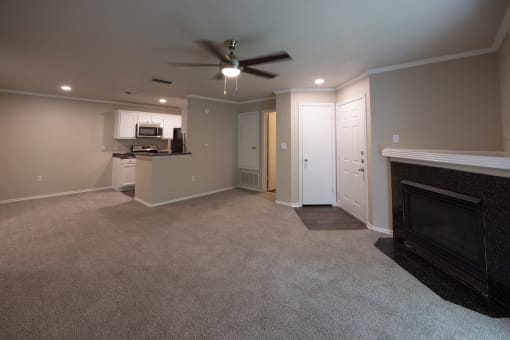 View of Tuscany from living area with carpet flooring, gas fireplace, ceiling fan and view of kitchen with white cabinets, dark counters, and stainless appliances.