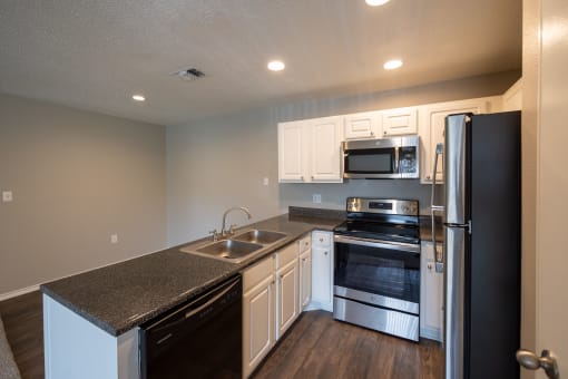 View of open kitchen and dining with dark counters, stainless and black appliances, white cabinets, and wood look flooring