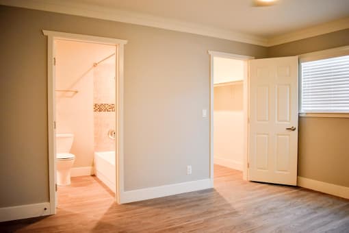 View of bedroom with wood-like flooring with a view into the connecting bathroom and a view into the walk in closet