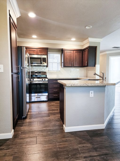 Kitchen view with brown cabinets, stone counters, tile backsplash, and stainless appliances