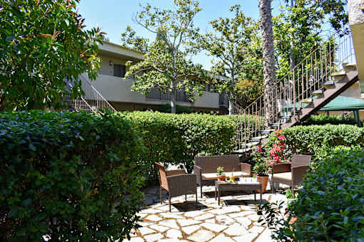 A patio with a table and chairs surrounded by greenery.