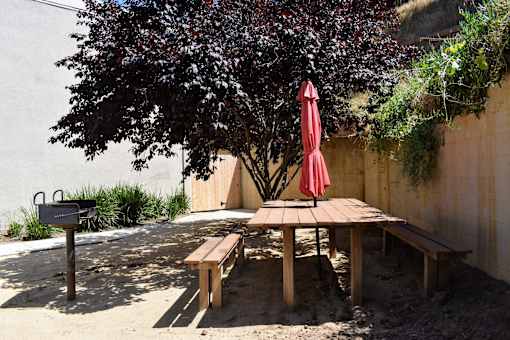 A red umbrella is on a wooden table under a tree.
