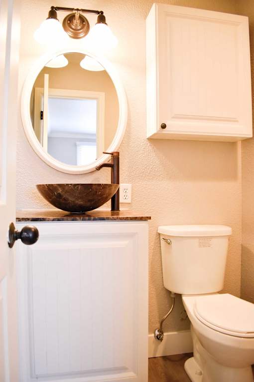 A white toilet sits next to a white cabinet and a round mirror above a sink.