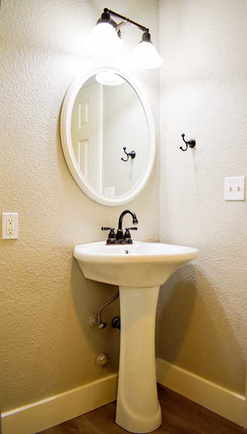 A white pedestal sink with a round mirror above it.