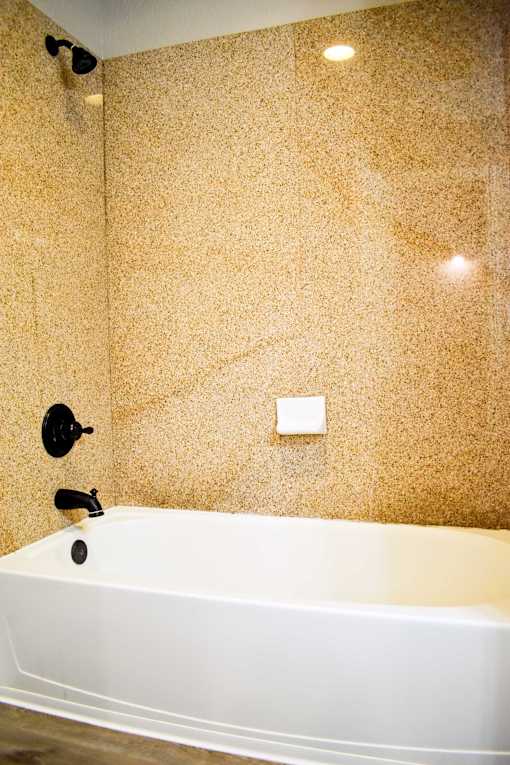 A white bathtub sits in a bathroom with a brown speckled wall.