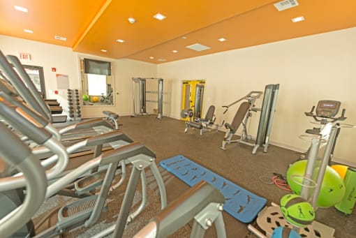 a gym with cardio equipment and weights in a wellness center at Midtown Sam Houston Apartments, Huntsville, Texas