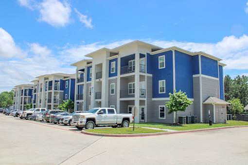 A large blue and white apartment complex with a parking lot in front.