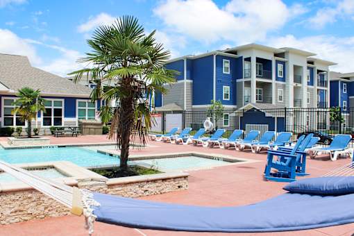A pool surrounded by chairs and a hammock in front of a building.