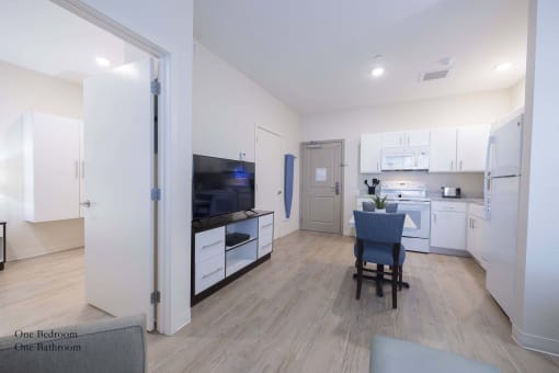 a living room and kitchen with white cabinets and a table with a chair at Parks Residential - Richardson, Richardson