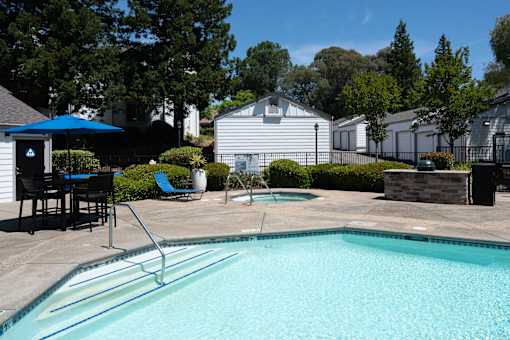 A swimming pool with a blue umbrella and a white house in the background.
