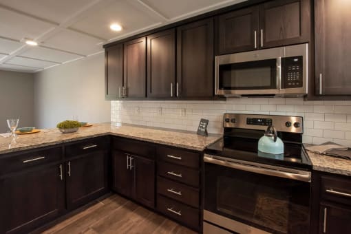 view of kitchen with stone counters, tile backsplash, stainless appliances, brown cabinets, and wood look flooring