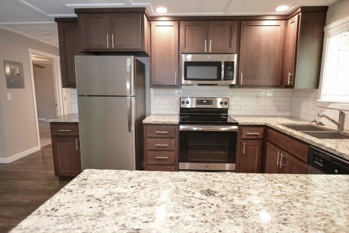 Alternate view of kitchen with stone counters, tile backsplash, brown cabinets, stainless appliances, recessed lighting, and wood like flooring