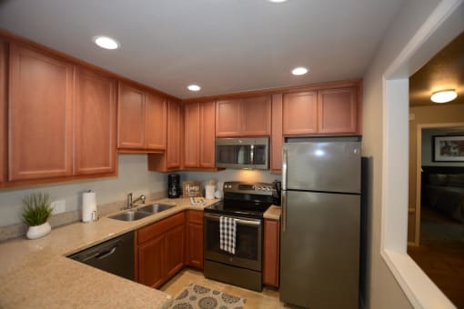 View of kitchen with stone counters, stainless appliances, brown cabinets