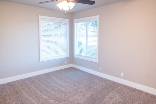 an empty room with two windows and a ceiling fan