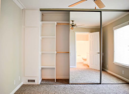 View of large sliding glass mirror door closet with built in shelving and carpet in bedroom