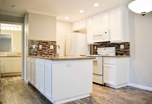 View of kitchen with wood look flooring, stainless appliances, tile backsplash, and white cabinets