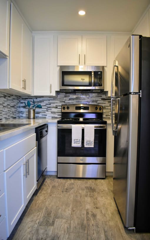 View of kitchen with stainless appliances, stone counter tops, white cabinets and recessed lighting