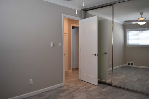 View of bedroom with sliding glass mirror closet with view of well lit window and ceiling fan.