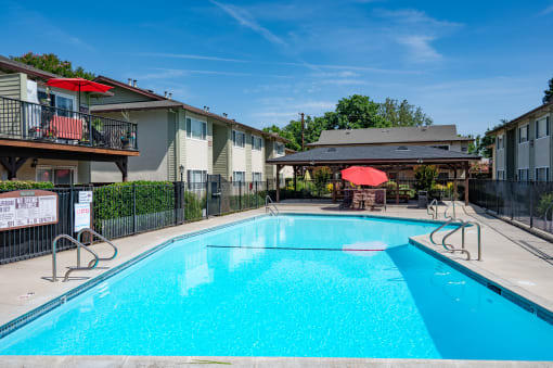 View of gated community pool with seating under umbrellas and covered area with seating and picnic table