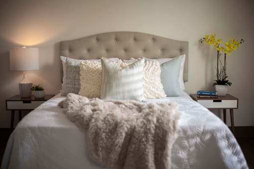 A bed with a white comforter and pillows with a white fluffy throw on it.