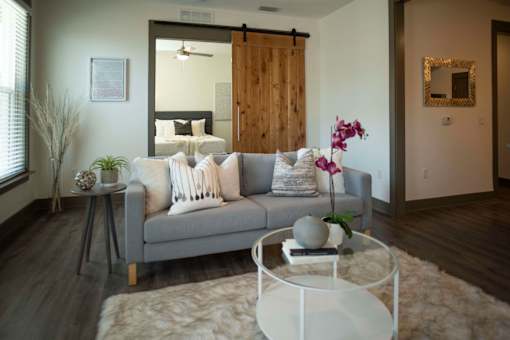 A grey couch with pillows and a grey and white throw is in the middle of a room with a white coffee table in front of it.