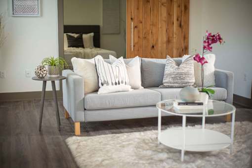 A grey couch with white pillows and a white coffee table in front of it.